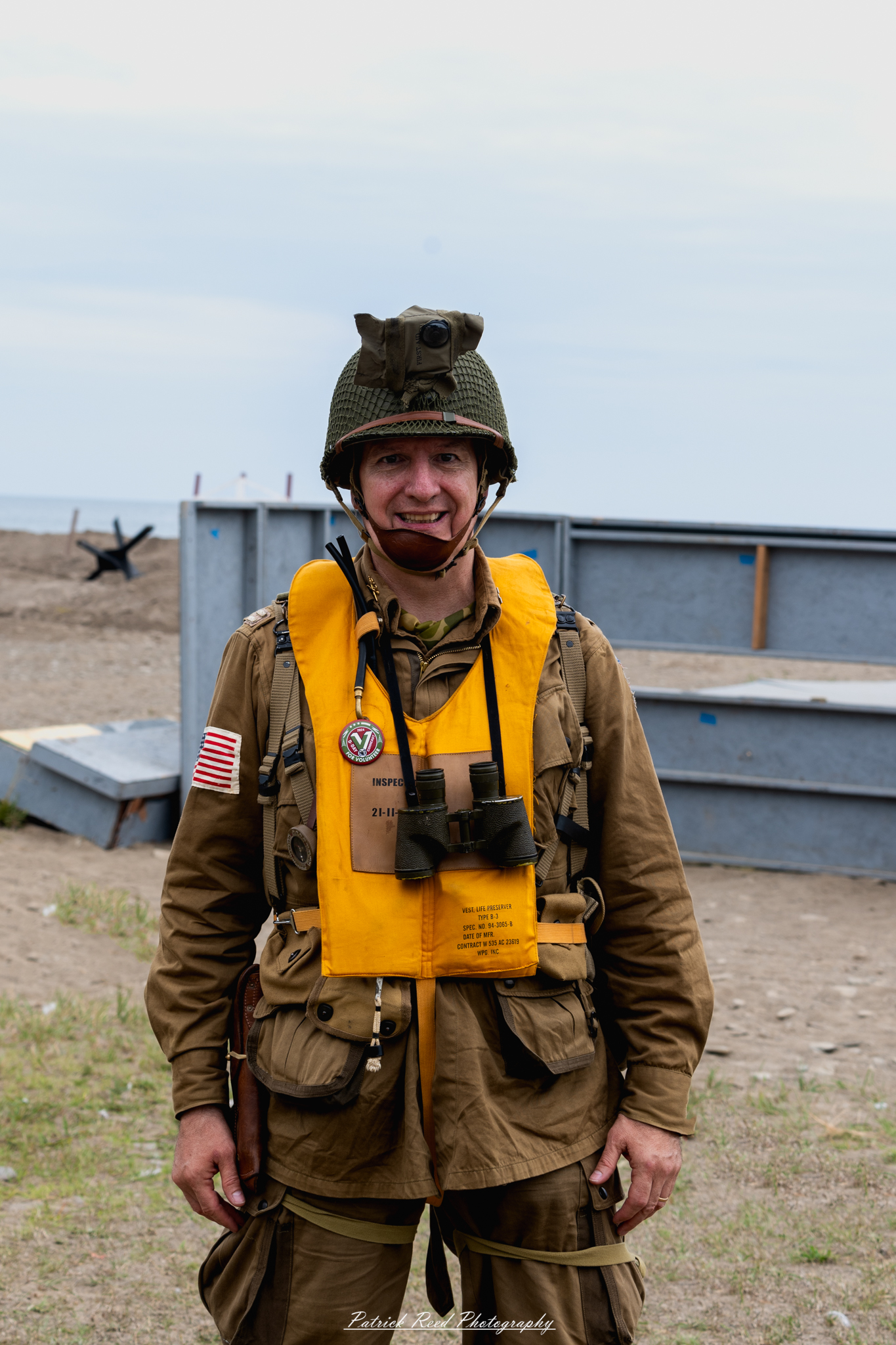 "A US World War II soldier dressed in full uniform, wearing a life preserver over his gear. The soldier's uniform is neatly pressed, with patches and insignia visible, indicating his rank and unit. The life preserver is strapped securely across his chest, preparing him for amphibious operations or sea transport. His expression is focused and determined, embodying the bravery and readiness of the time. The background features a muted, military setting, enhancing the historical significance of the scene."